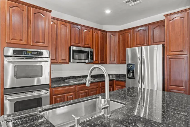 a kitchen with kitchen island granite countertop wooden cabinets a refrigerator a stove a dining table and chairs