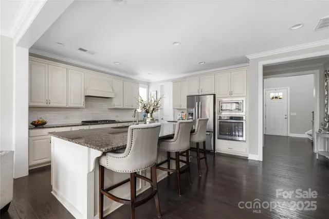 a kitchen with stainless steel appliances granite countertop a table chairs refrigerator and sink