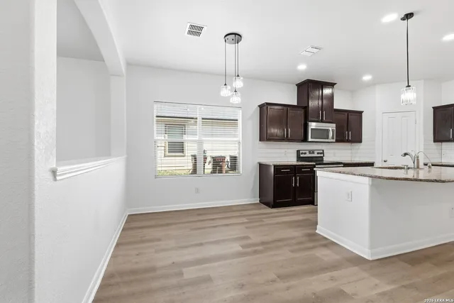 a kitchen with stainless steel appliances kitchen island granite countertop a stove top oven a sink a microwave and wooden floors