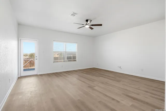an empty room with wooden floor chandelier fan and windows