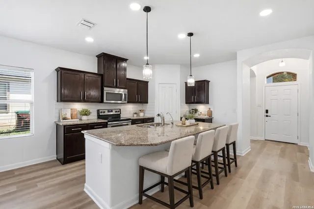 a kitchen with stainless steel appliances granite countertop a stove top oven a sink dishwasher a dining table and chairs with wooden floor