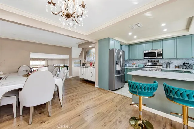 a kitchen with stainless steel appliances granite countertop a refrigerator a stove a sink a dining table and chairs with wooden floor