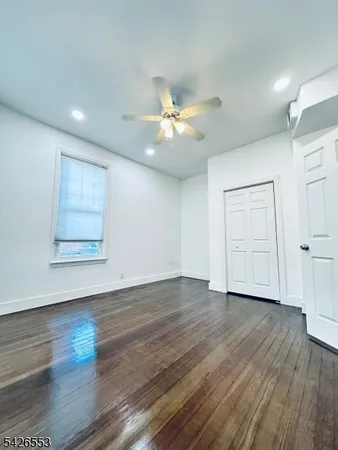 a view of an empty room with wooden floor and a ceiling fan