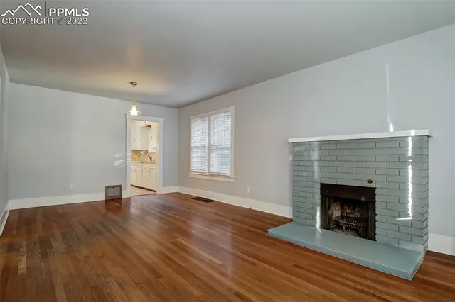 a view of an empty room with wooden floor fireplace and a window