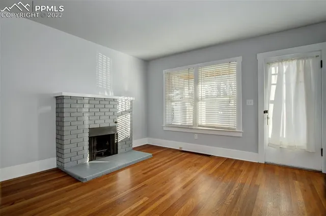 an empty room with wooden floor fireplace and windows