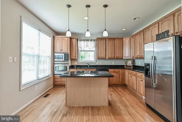 a kitchen with stainless steel appliances granite countertop a refrigerator a sink dishwasher a stove and white countertops with wooden floor