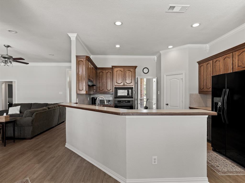 10066 Irish Ridge Forney, TX 75126 - Photo 19 of 39 Kitchen with black appliances, wood finished floors, a peninsula, backsplash, and under cabinet range hood