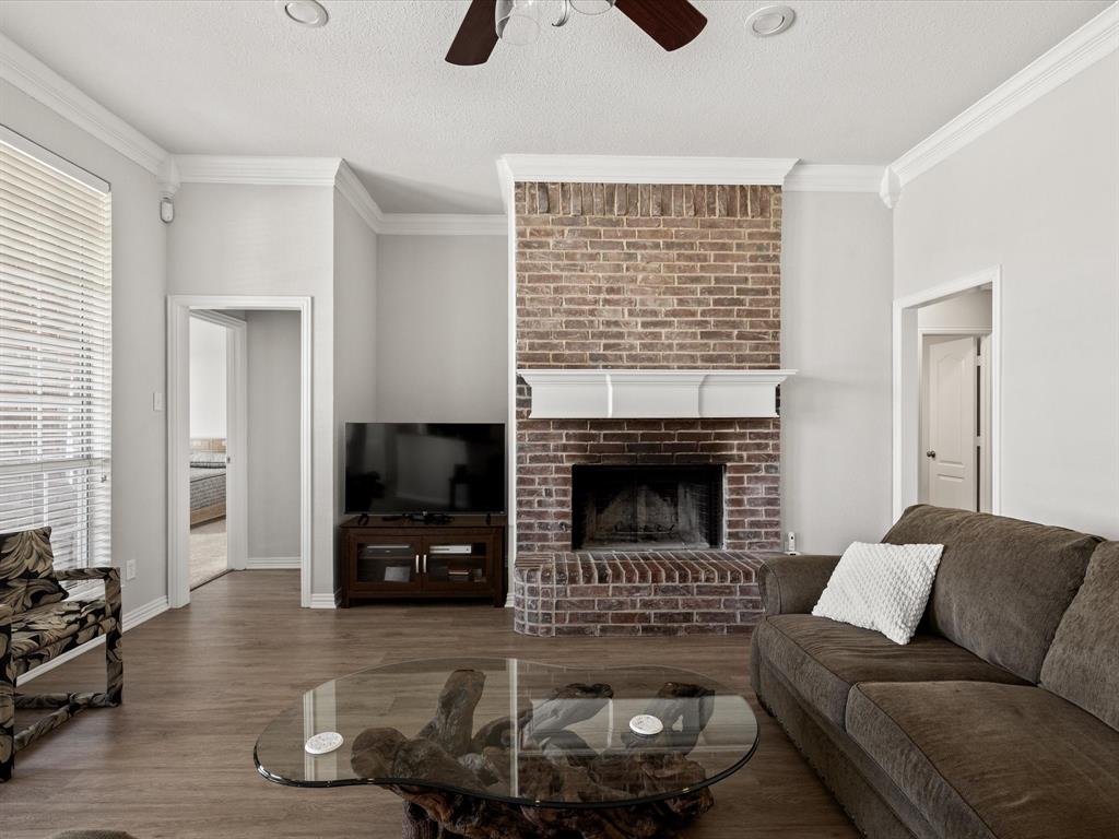 10066 Irish Ridge Forney, TX 75126 - Photo 3 of 39 Living area featuring a ceiling fan, crown molding, wood finished floors, a brick fireplace, and a textured ceiling
