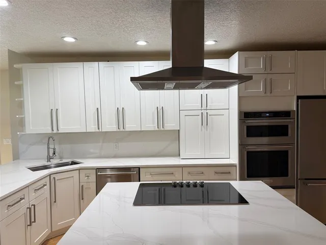 a kitchen with granite countertop a refrigerator a sink and white cabinets