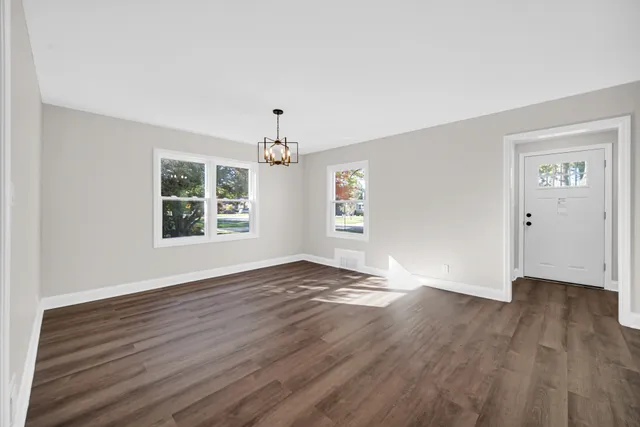 an empty room with wooden floor chandelier and windows
