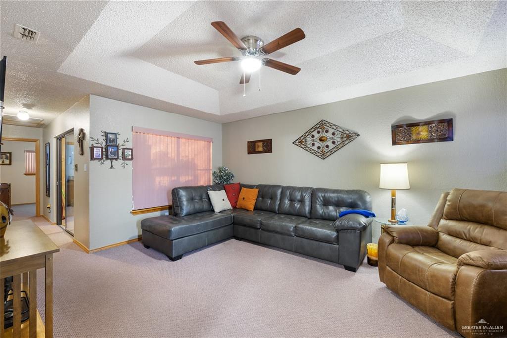 1804 Woodrow Street, Unit 184 Mission, TX 78572 - Photo 2 of 15 Living area featuring a textured ceiling, carpet, a tray ceiling, and a ceiling fan