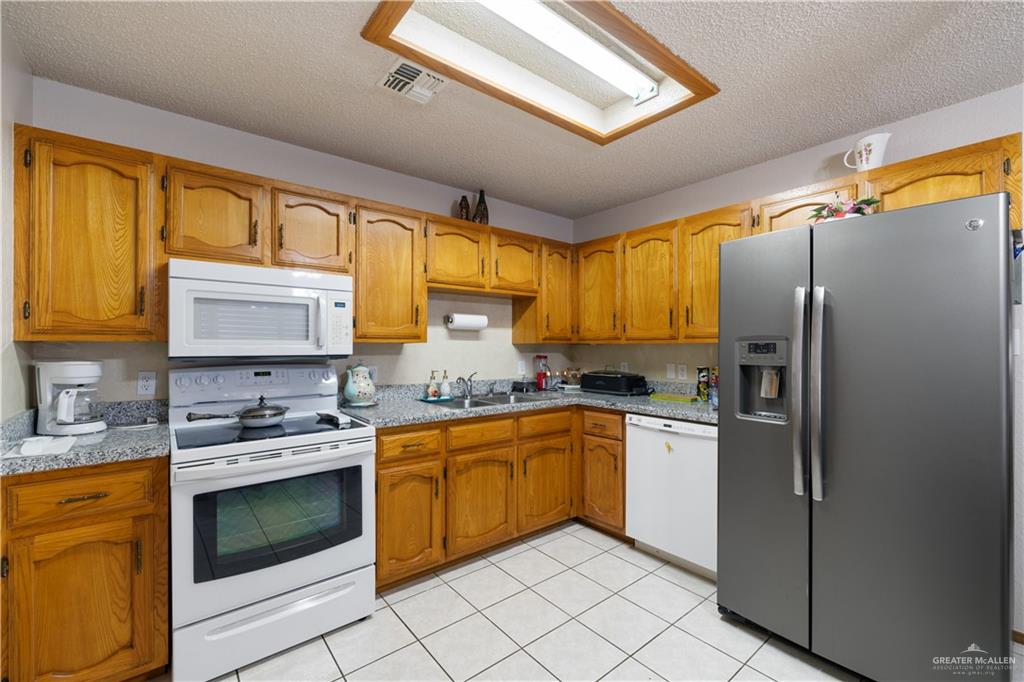 1804 Woodrow Street, Unit 184 Mission, TX 78572 - Photo 6 of 15 Kitchen with white appliances, a textured ceiling, brown cabinets, and light tile patterned floors