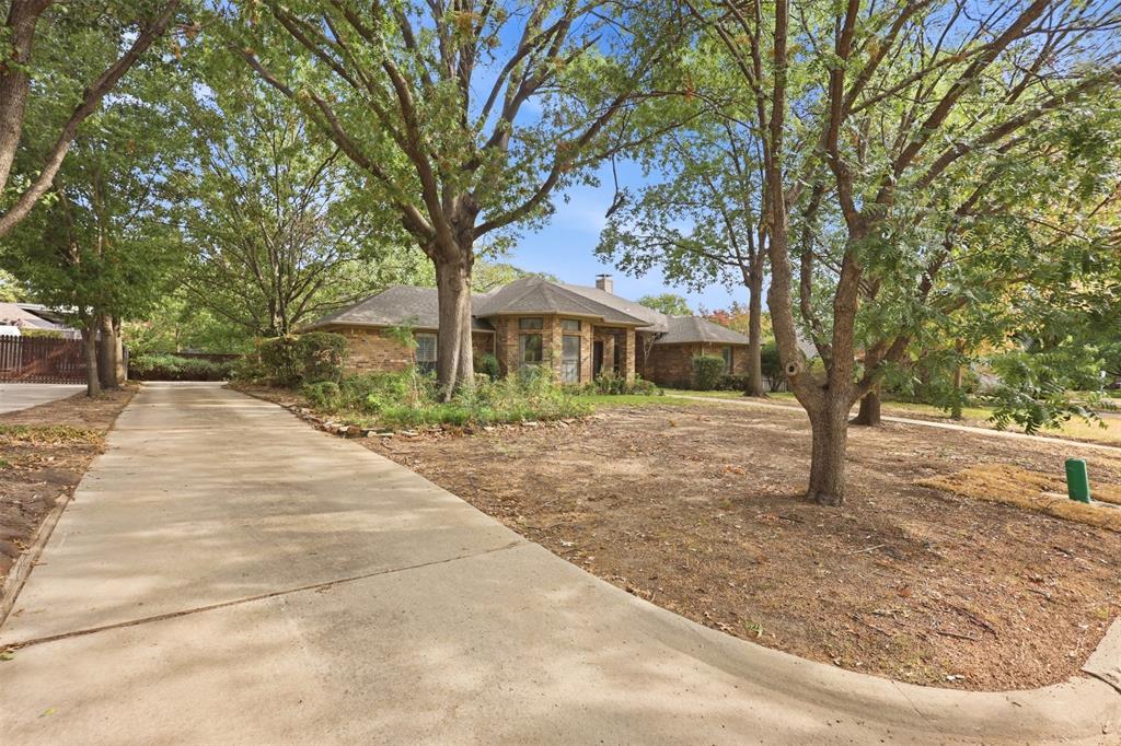 37 Timbergreen Circle Denton, TX 76205 - Photo 4 of 31 Concrete driveway leading to a stone and brick exterior home with mature trees and a sloped lawn