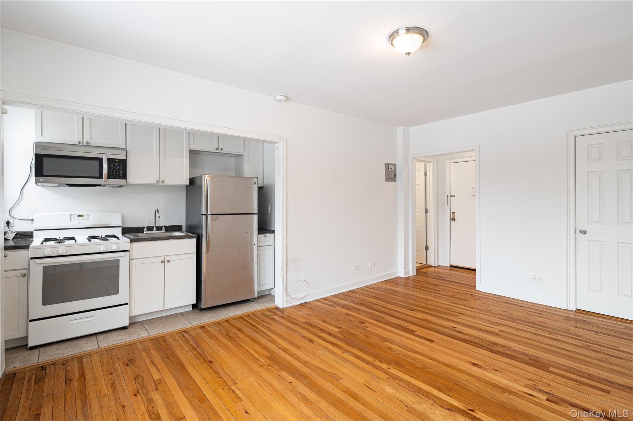 Kitchen with appliances with stainless steel finishes, light wood finished floors, dark countertops, and white cabinetry