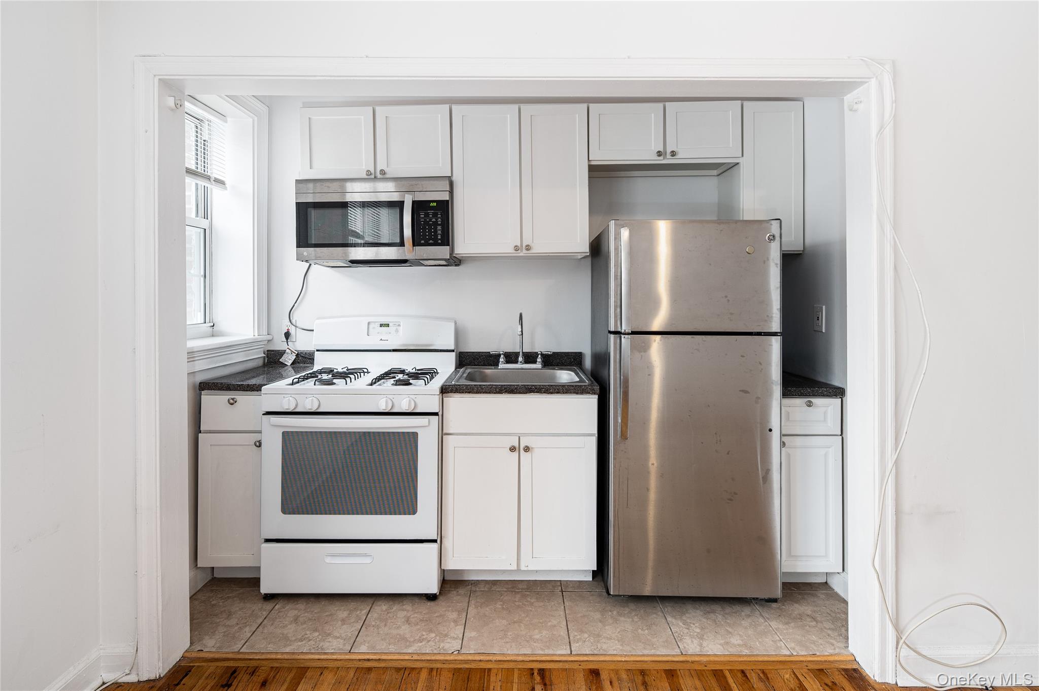 633 Old Post Road, Unit 32 Bedford, NY 10506 - Photo 2 of 10 Kitchen featuring stainless steel appliances, dark countertops, light wood-type flooring, and white cabinets