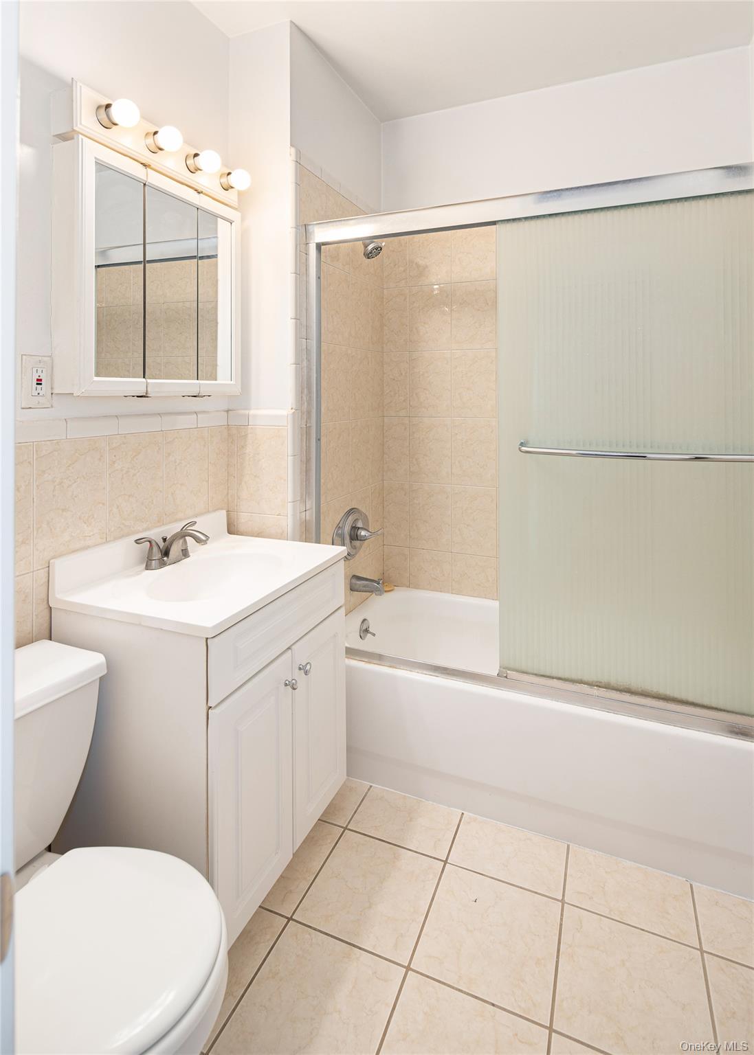 633 Old Post Road, Unit 32 Bedford, NY 10506 - Photo 4 of 10 Bathroom featuring vanity, bath / shower combo with glass door, tile walls, light tile patterned flooring, and a wainscoted wall