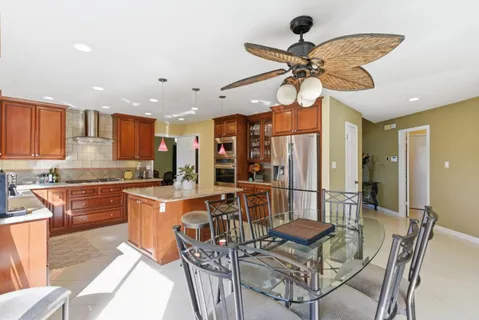 a kitchen with stainless steel appliances kitchen island granite countertop a refrigerator a stove a sink a dining table and chairs with wooden floor