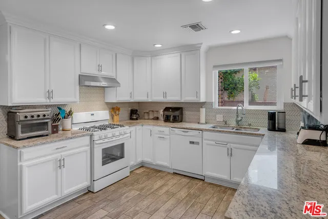 a kitchen with white cabinets appliances wooden floor and a window