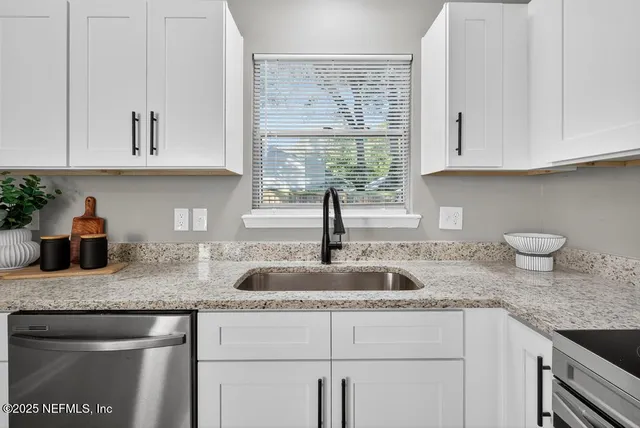 a kitchen with granite countertop a sink white cabinets and window