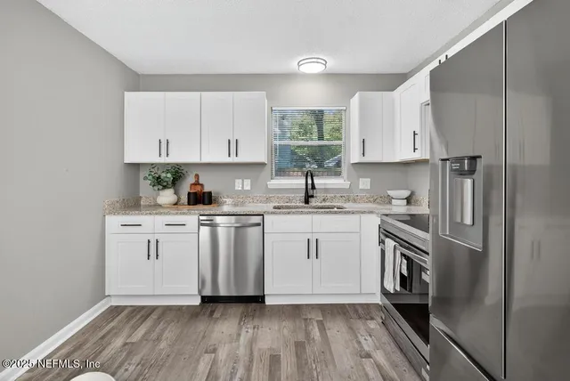 a kitchen with granite countertop a sink cabinets stainless steel appliances and a window