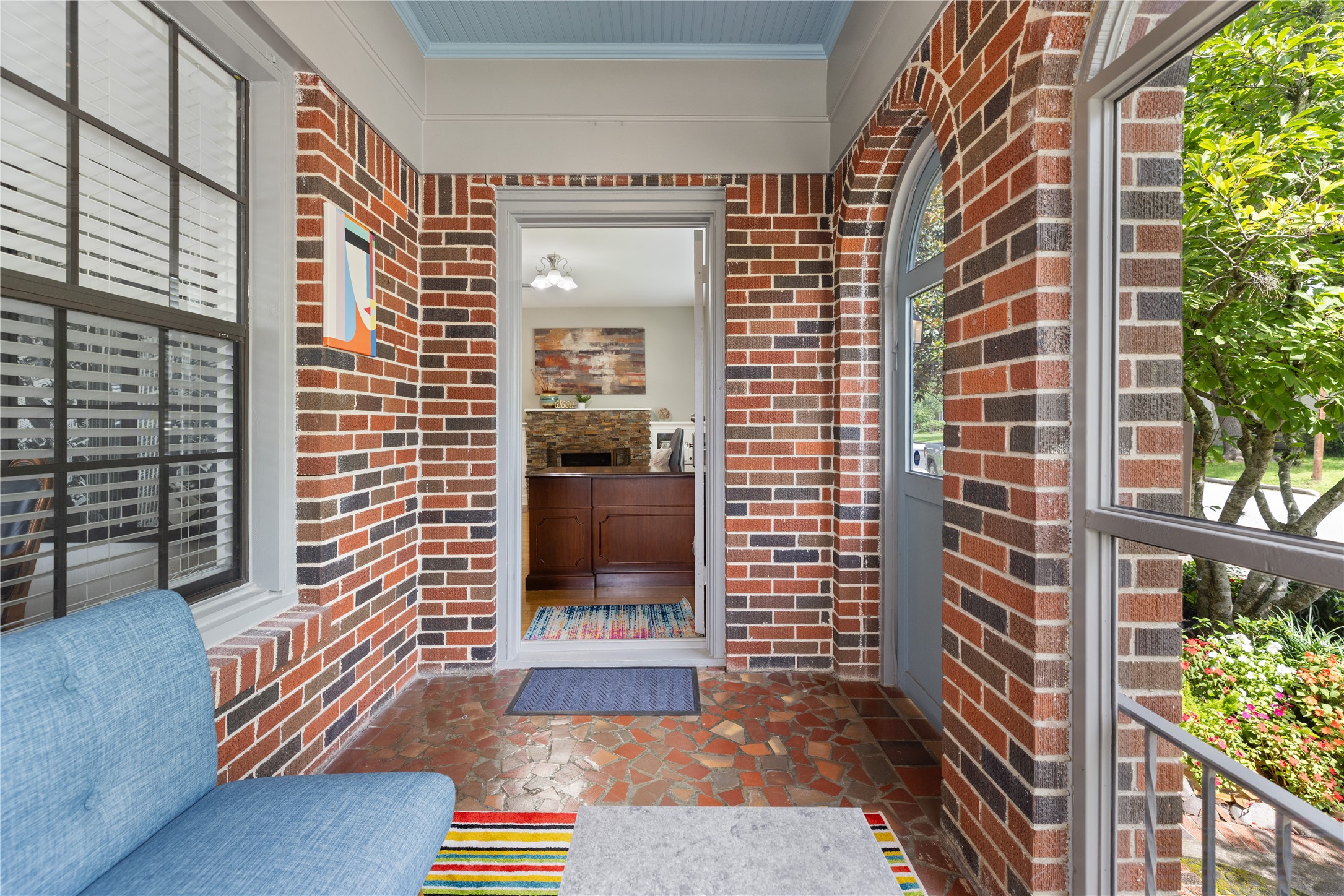 906 Higgins Street Humble, TX 77338 - Photo 19 of 26 Charming entryway with brick walls and arched windows, featuring a cozy sitting area and a view into a well-lit, inviting interior space. Perfect for enjoying the view of the garden.