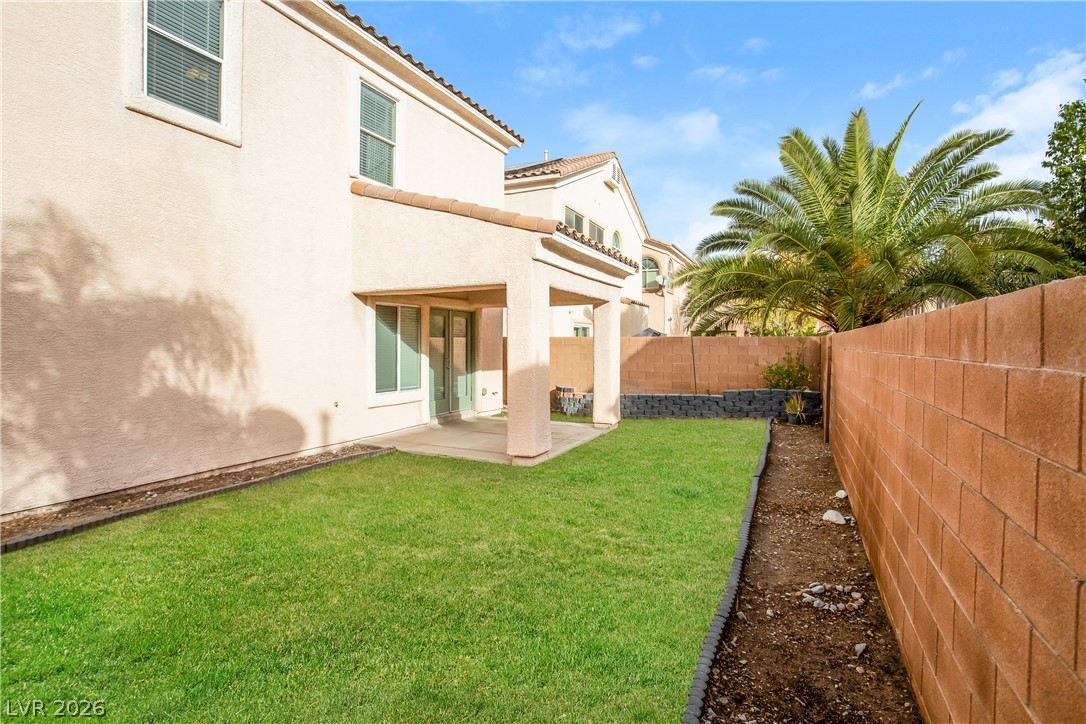 7630 Riva Ridge Street Las Vegas, NV 89149 - Photo 13 of 14 Green lawn and a covered concrete patio are enclosed by a privacy block wall.