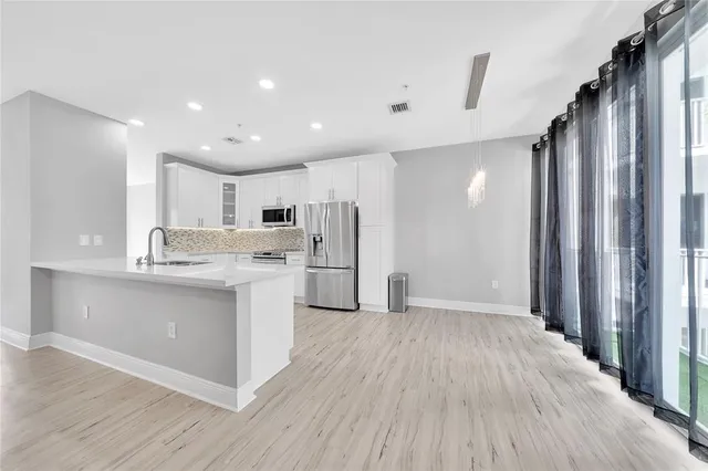 a large white kitchen with a refrigerator a sink dishwasher a stove and a dining table with wooden floor