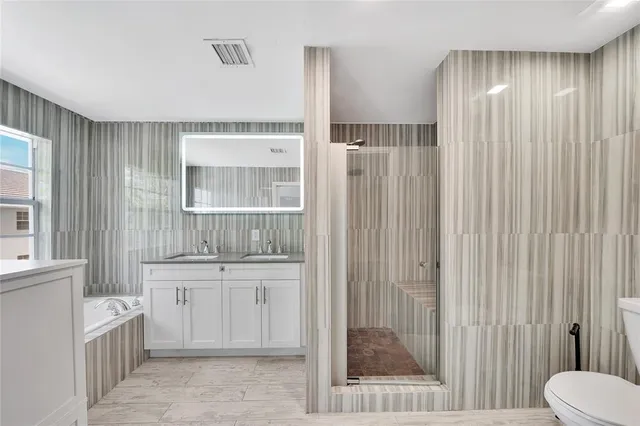 a bathroom with a bathtub shower sink vanity mirror and toilet