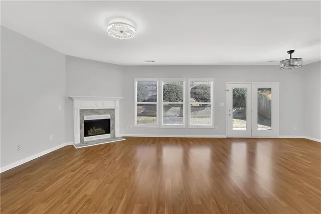 an empty room with wooden floor chandelier fan and windows