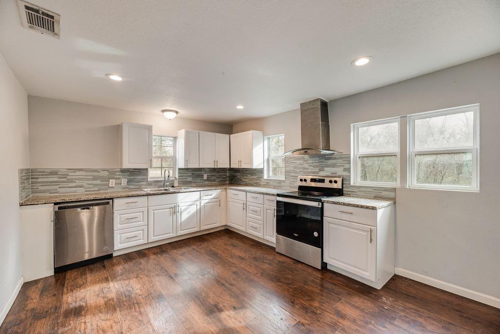 500 East Main Street Denison, TX 75021 - Photo 2 of 21 Kitchen featuring stainless steel appliances, white cabinets, decorative backsplash, dark wood-style flooring, and light stone countertops