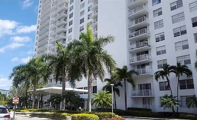 a front view of a multi story building with yard and palm trees