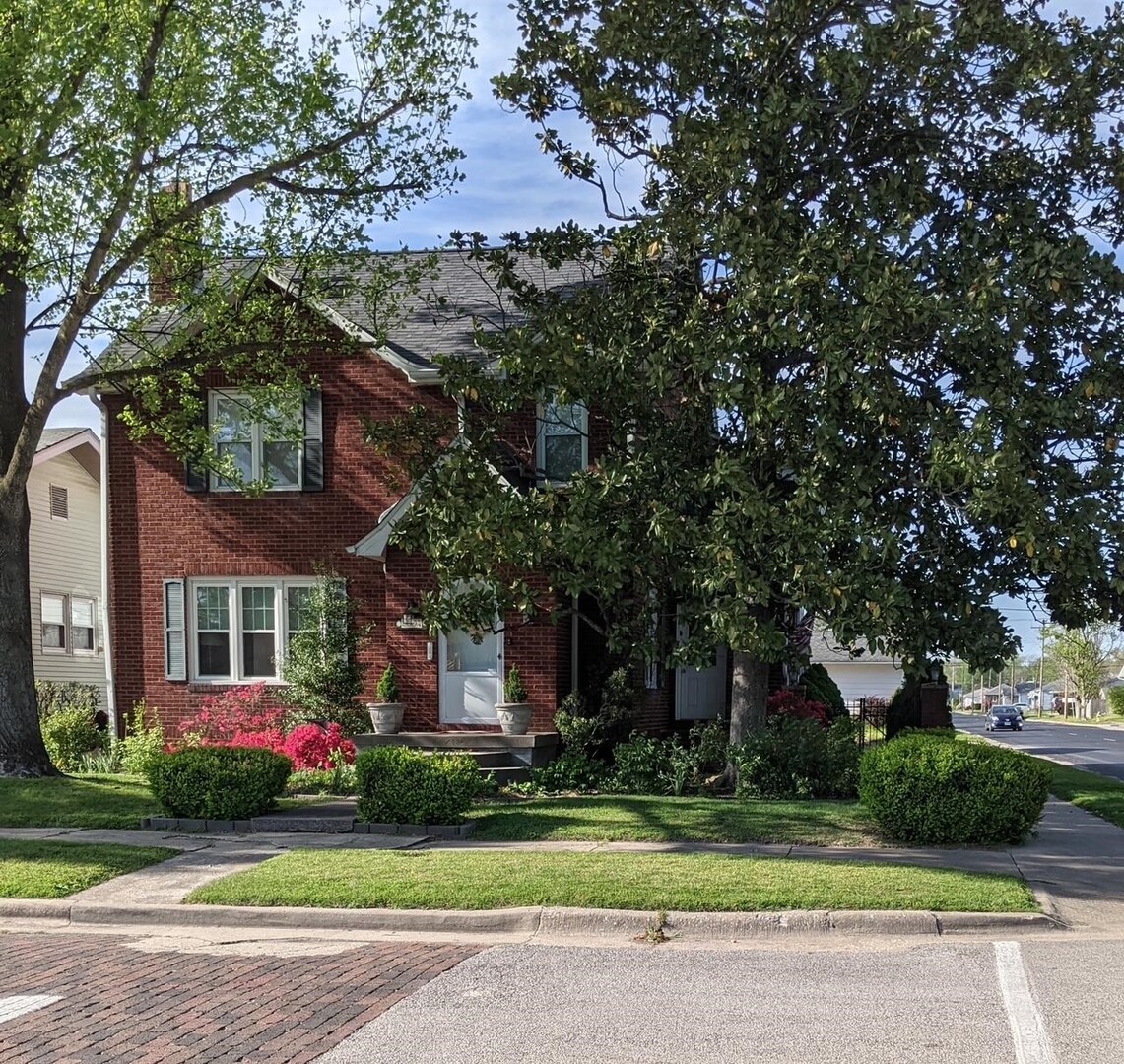 a front view of a house with a garden and trees
