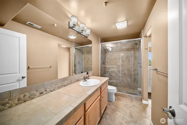 a bathroom with a granite countertop sink a toilet a mirror and shower