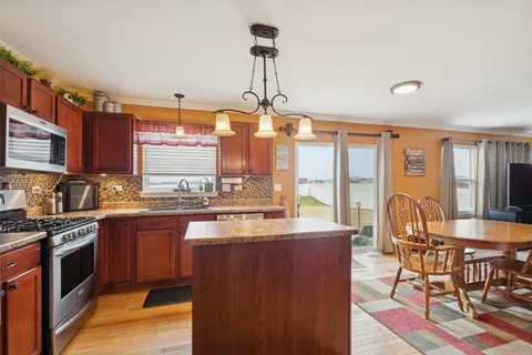 a kitchen with stainless steel appliances granite countertop a stove top oven a sink dishwasher a dining table and chairs with wooden floor