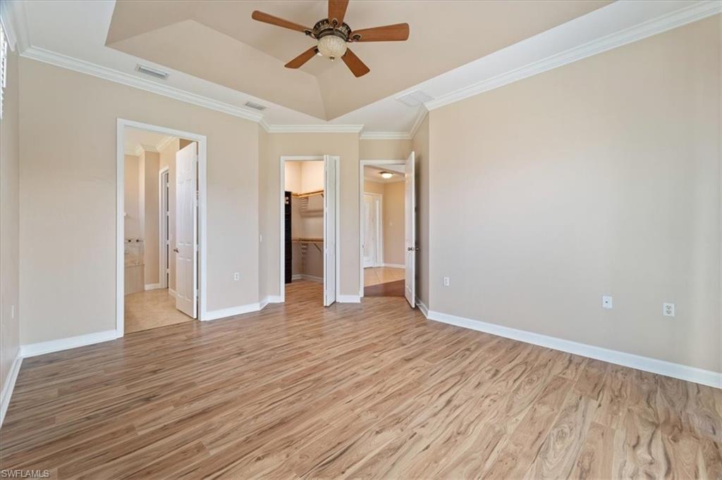 3343 Sandpiper Way Naples, FL 34109 - Photo 10 of 31 Unfurnished bedroom featuring ensuite bath, a raised ceiling, ceiling fan, light hardwood / wood-style flooring, and a spacious closet