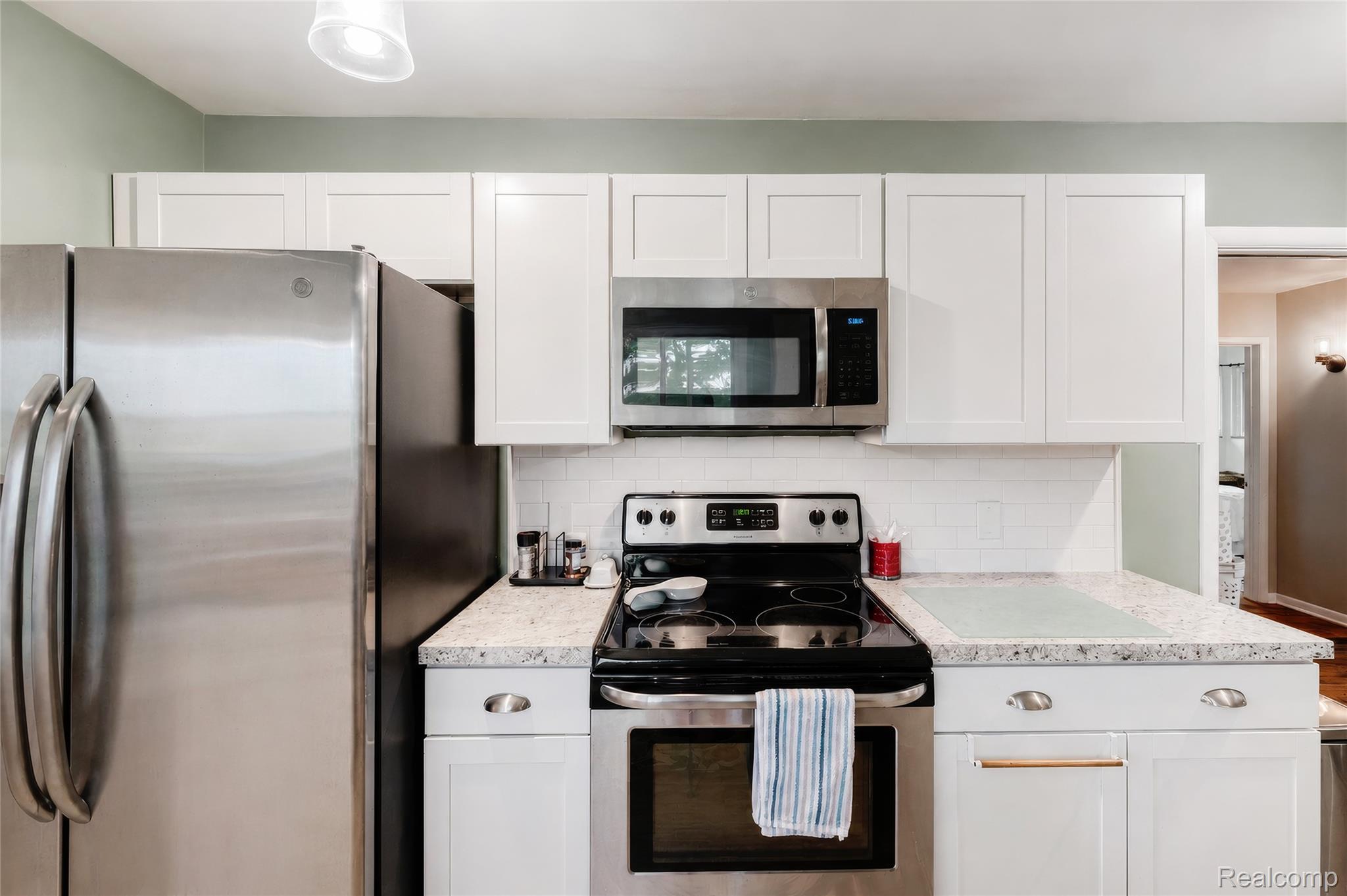 4499 South Linden Road Flint, MI 48507 - Photo 16 of 36 Stainless steel appliances, white shaker-style cabinetry, subway tile backsplash, and light-toned countertops