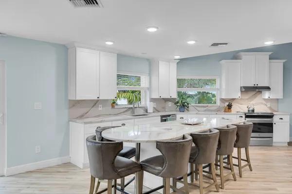 a kitchen with stainless steel appliances kitchen island granite countertop a sink a stove a refrigerator cabinets and chairs