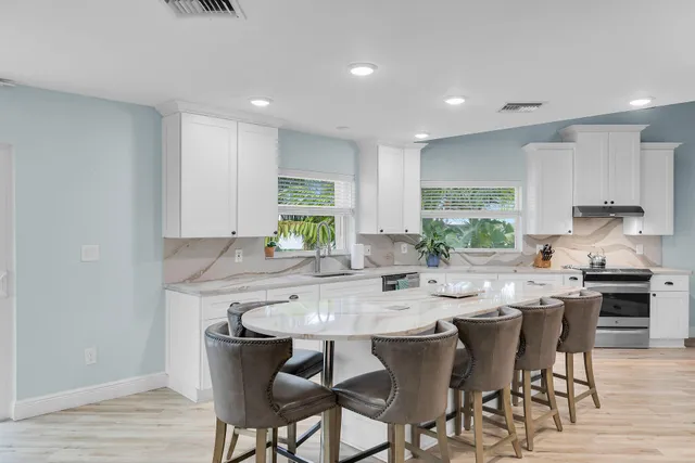 a kitchen with stainless steel appliances kitchen island granite countertop a sink a stove a refrigerator cabinets and chairs