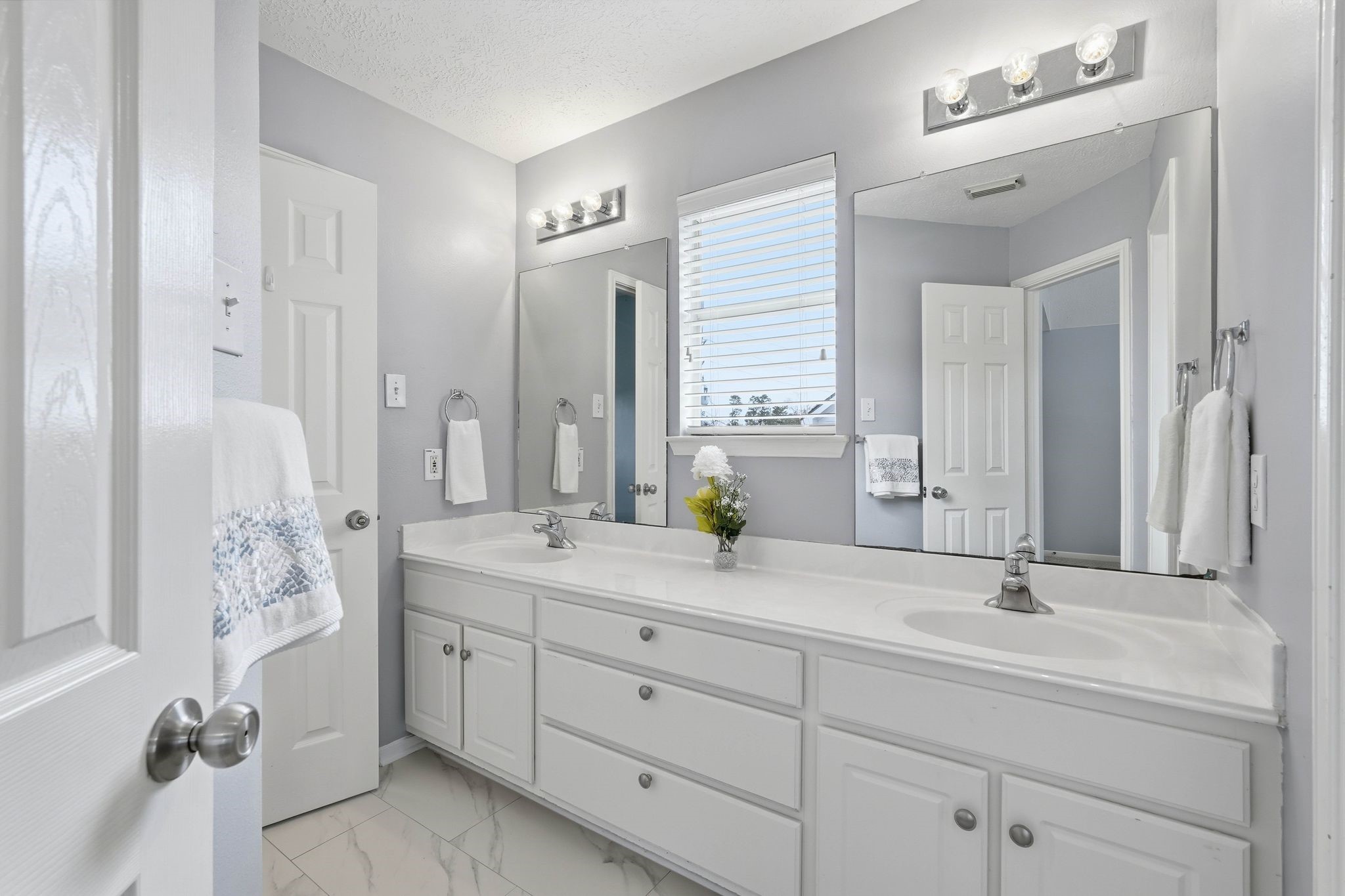2515 Woodsboro Drive Spring, TX 77388 - Photo 32 of 44 This bathroom features a modern, clean design with a double vanity, ample storage in white cabinets, and large mirrors. It has sleek lighting fixtures, a neutral color palette, and polished tile flooring, creating a bright and inviting space.