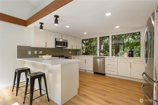 a kitchen with stainless steel appliances kitchen island granite countertop a stove a sink a refrigerator white cabinets and wooden floor