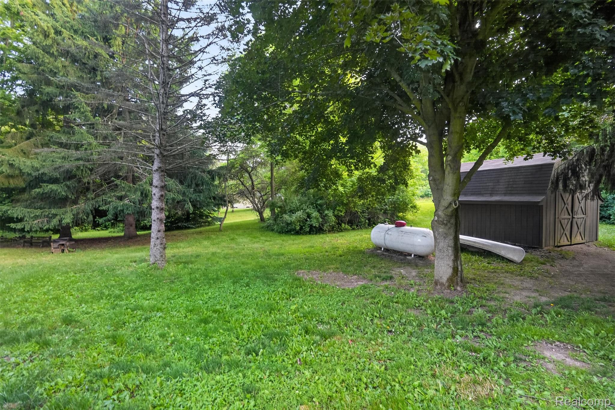 16955 English Road Manchester, MI 48158 - Photo 34 of 37 Expansive grassy yard with mature trees, featuring a wooden storage shed with barn doors and a dark shingle roof