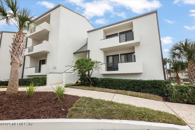 a view of swimming pool that has lawn chairs with plants and palm trees