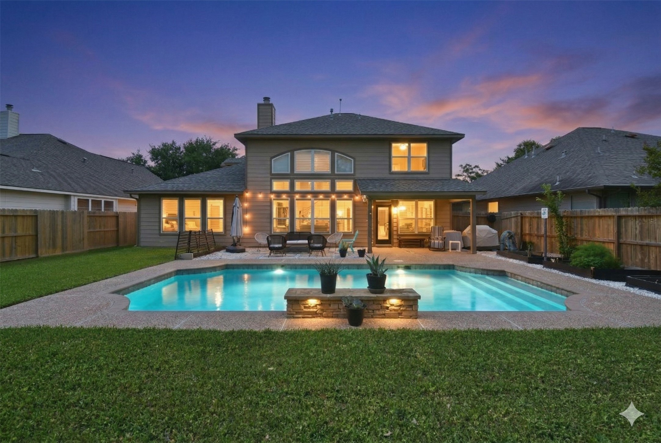 Resort-style backyard featuring a sparkling pool with a custom water feature, spacious patio seating area and beautifully maintained lawn, all set against a stunning twilight backdrop.
