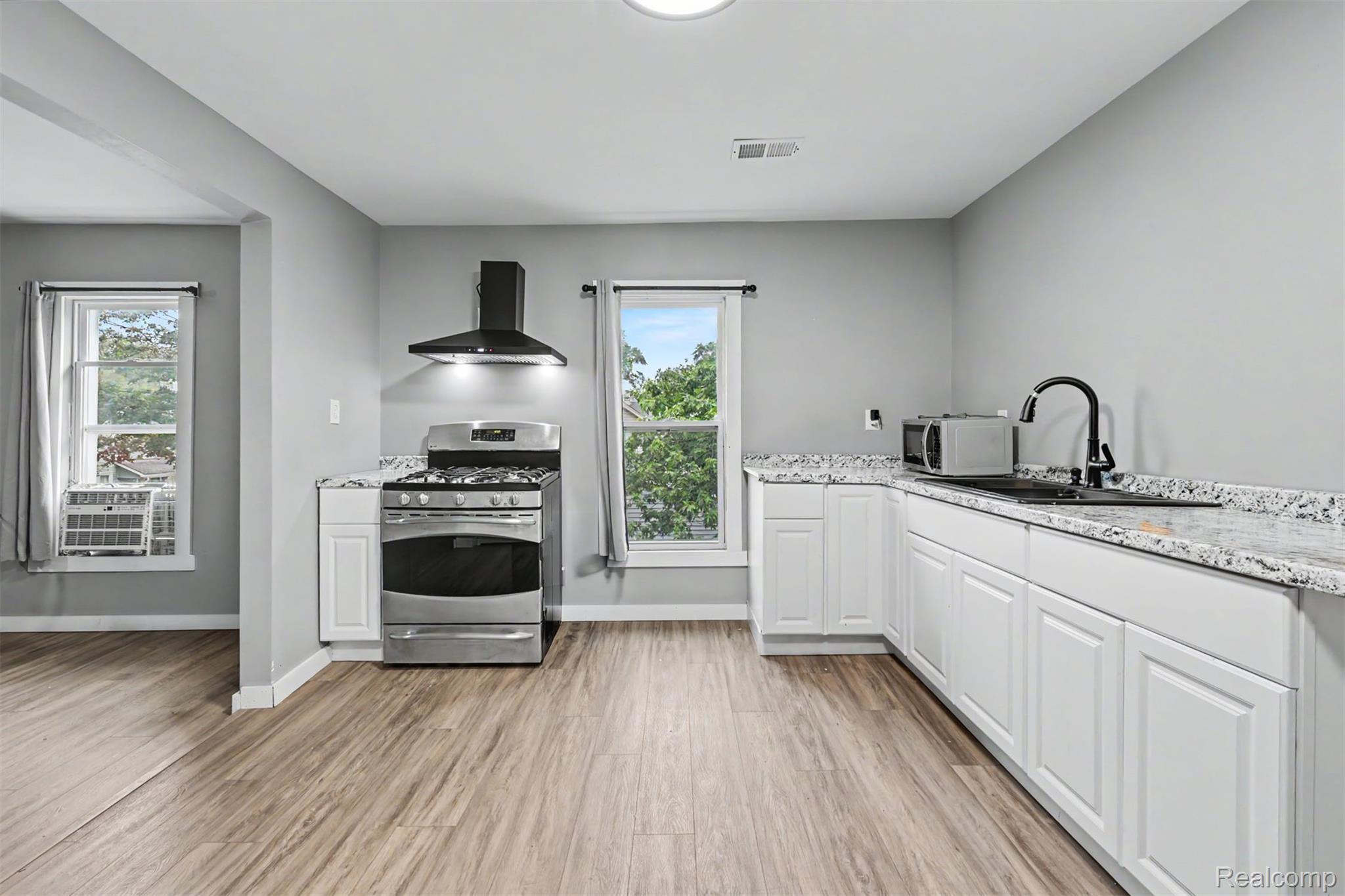 8397 Lane Street Detroit, MI 48209 - Photo 26 of 41 White shaker-style cabinetry with dark hardware, stainless steel gas range with a black range hood, light-toned wood-finish flooring, and light-toned countertops