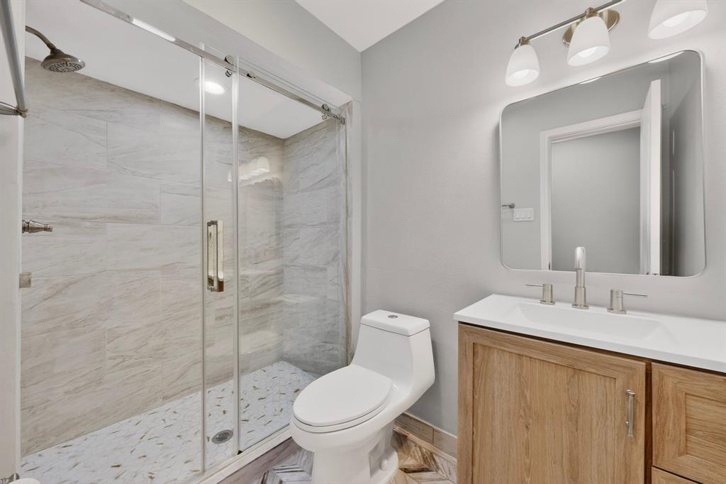 7631 Meadow Road Dallas, TX 75230 - Photo 16 of 40 A modern bathroom showcasing a shower stall, a toilet and a vanity, designed with light colors and ample space.