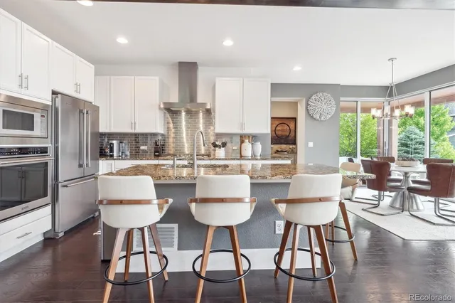 a kitchen with stainless steel appliances kitchen island granite countertop a dining table chairs and a refrigerator