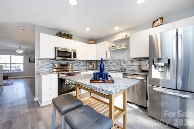 a kitchen with stainless steel appliances granite countertop a stove a sink a refrigerator a microwave and white cabinets