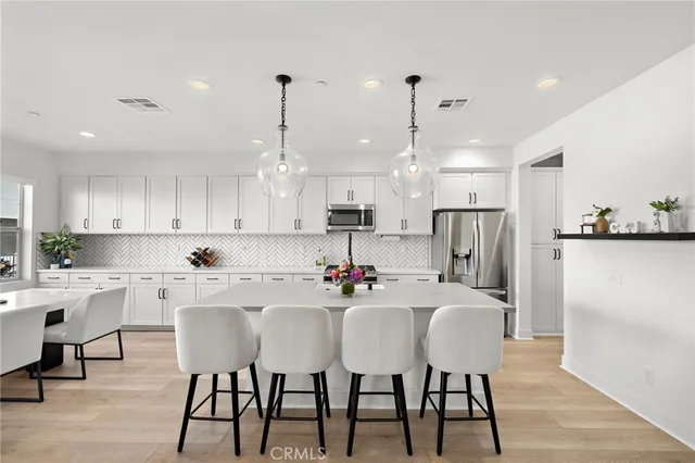 a kitchen with stainless steel appliances kitchen island granite countertop a dining table chairs and white cabinets
