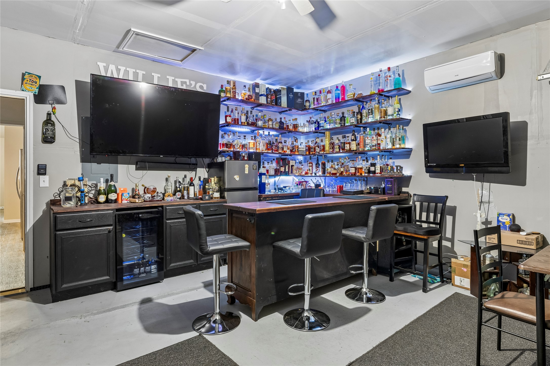 14409 Estuary Road Manor, TX 78653 - Photo 23 of 24 Dedicated entertainment space featuring a built-in bar, extensive shelving with integrated lighting, a beverage refrigerator, and two wall-mounted televisions