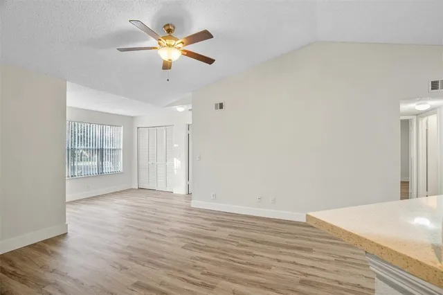a view of an empty room with wooden floor and a ceiling fan